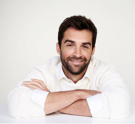 Image of a man in a white shirt and beard seated at a table against a white backdrop.